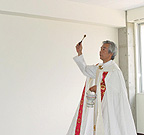 家の祝別で部屋に聖水を振りかける司祭